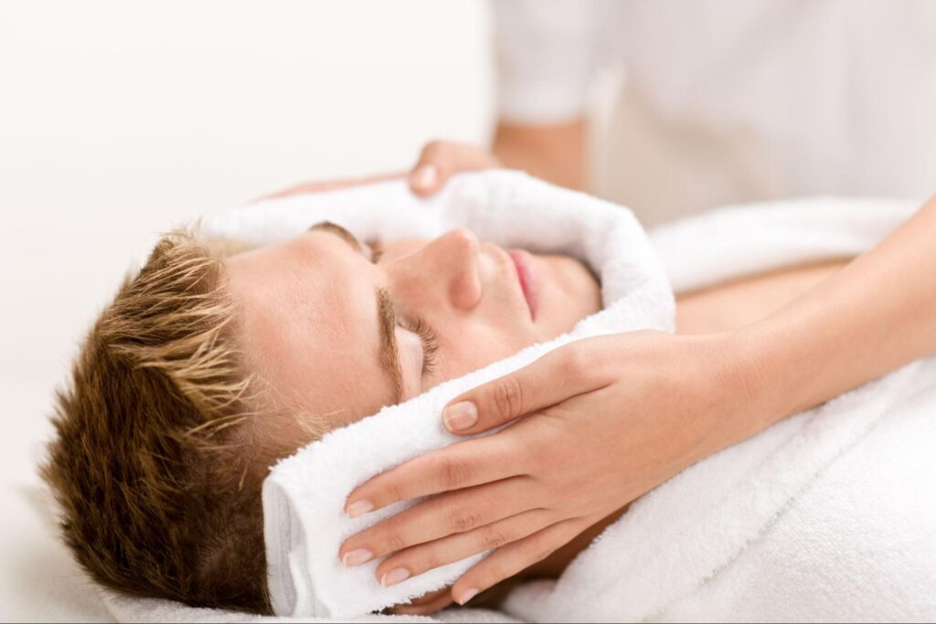 A man experiencing a facial treatment at a spa, with a towel applied to his face for cleansing and relaxation.