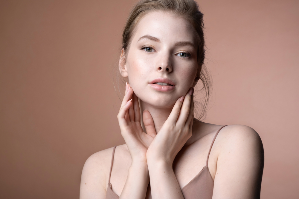 A young woman with glowing skin after a facial treatment, gently touching her face with a serene expression.