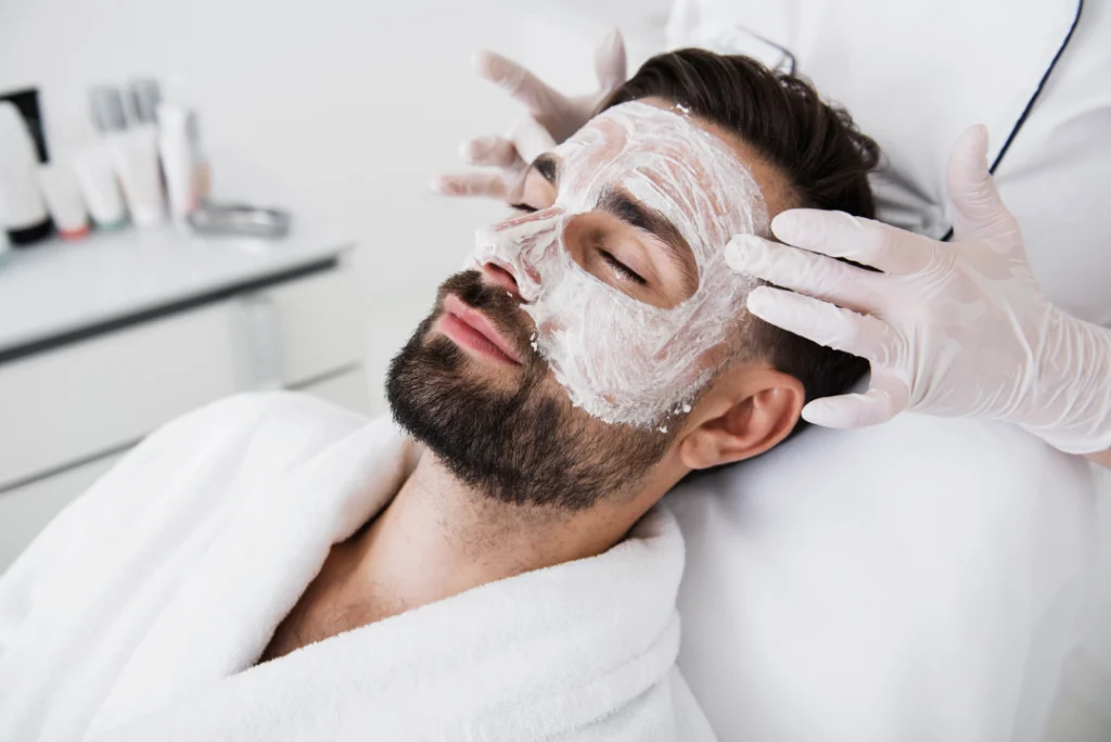 A man receiving a facial mask as part of acne treatments for men.