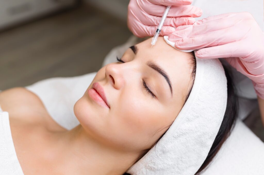 A woman receiving a Botox injection on her forehead from a professional wearing pink gloves.