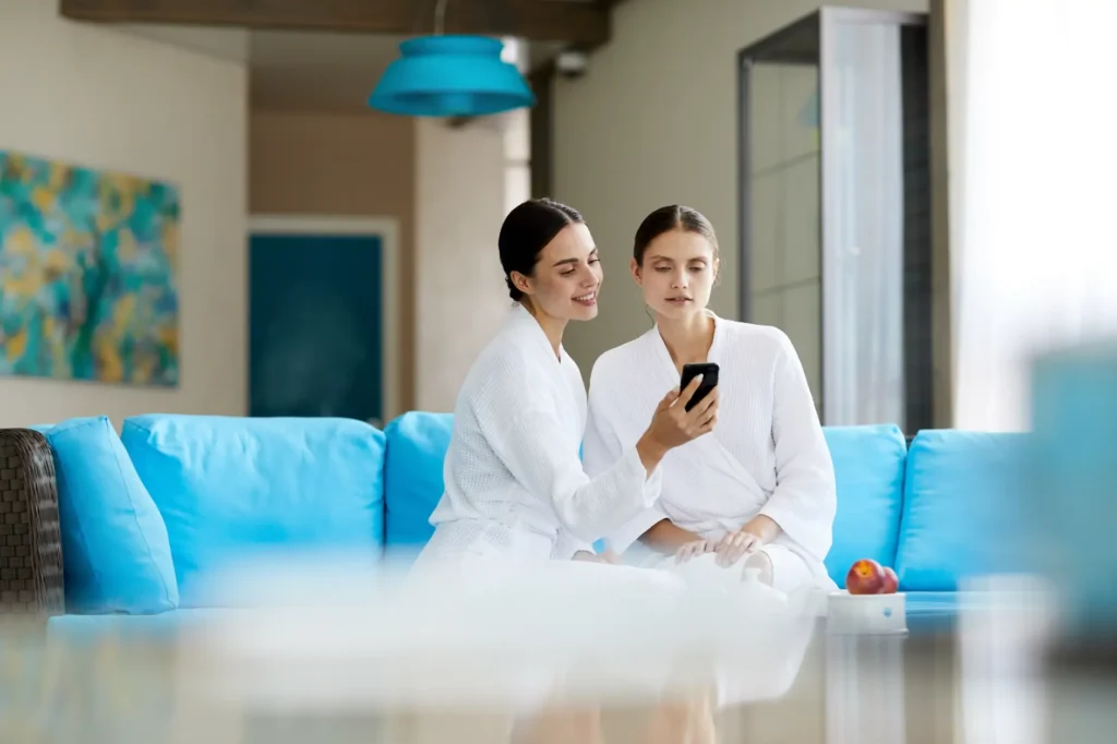 Two women in robes sitting on couch looking at phone together
