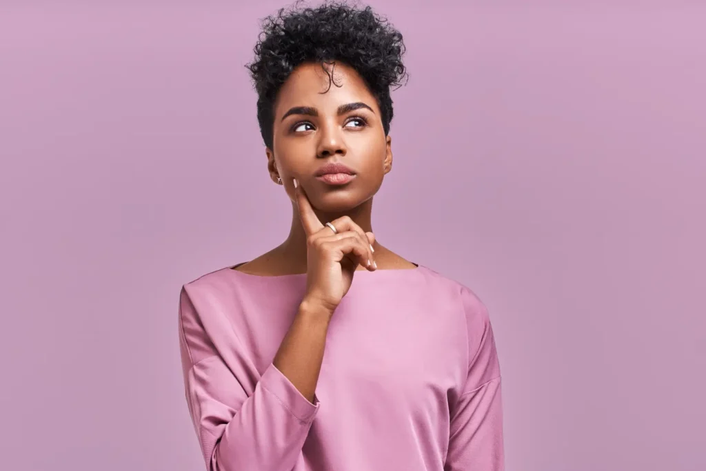 Woman in a pink top touching her chin while looking upward against a purple background