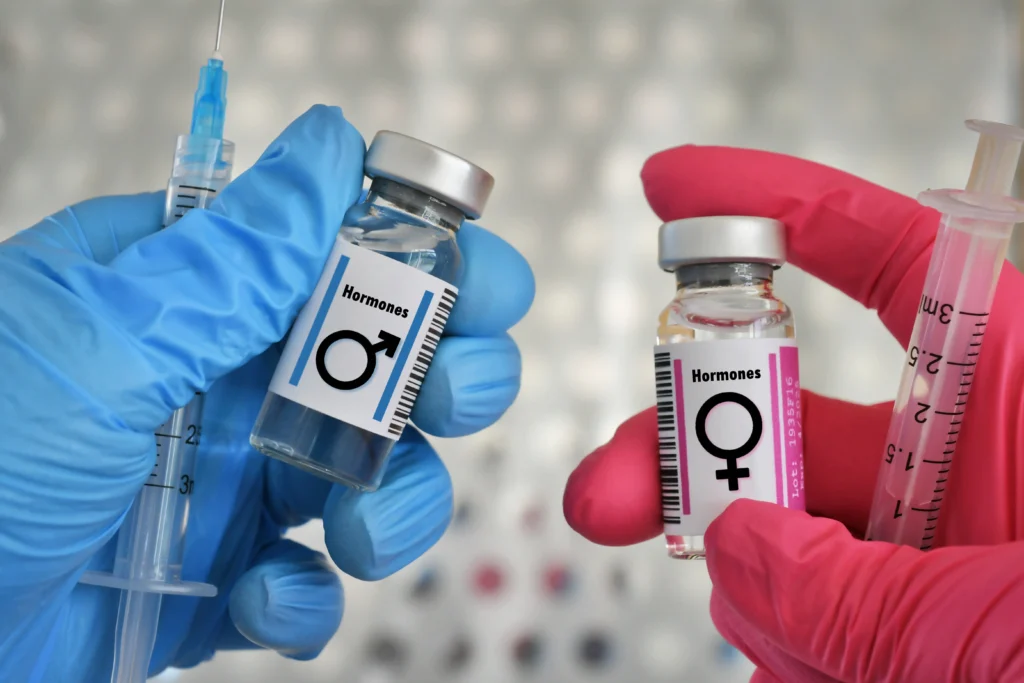 Two gloved hands hold hormone vials and syringes in a clinical setting