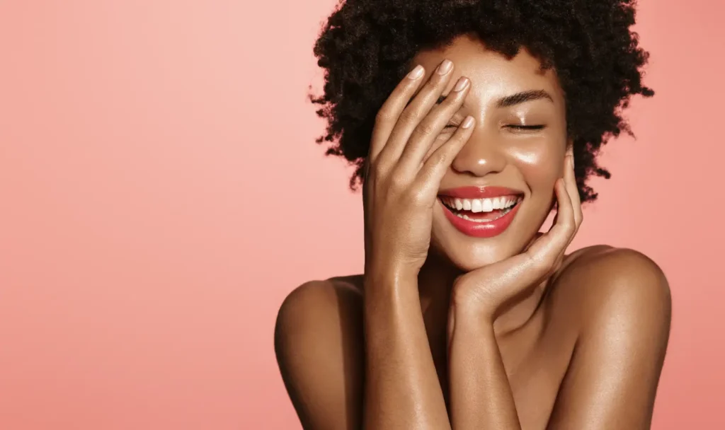 Smiling woman with curly hair posing against a pink background.