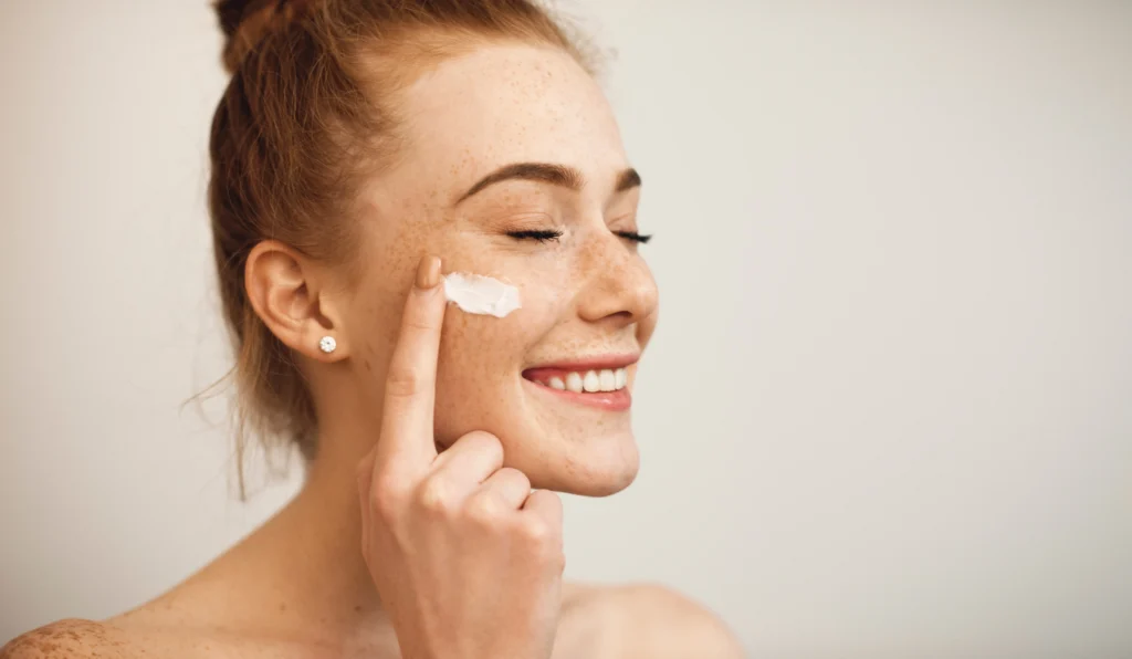 Woman smiling while applying cream to her cheek with one finger