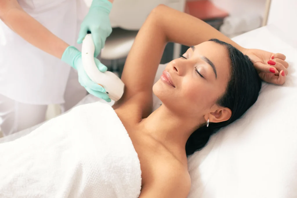 Patient receives laser hair removal treatment on the underarm while lying on a treatment bed.