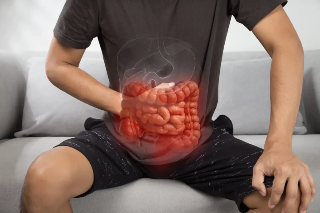 Seated person holds their abdomen with a digestive system illustration over the stomach area.