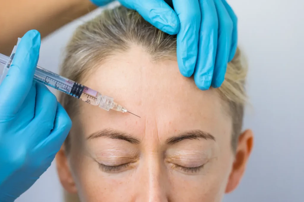 Gloved practitioner positions a syringe near a woman's forehead while supporting the top of her head.